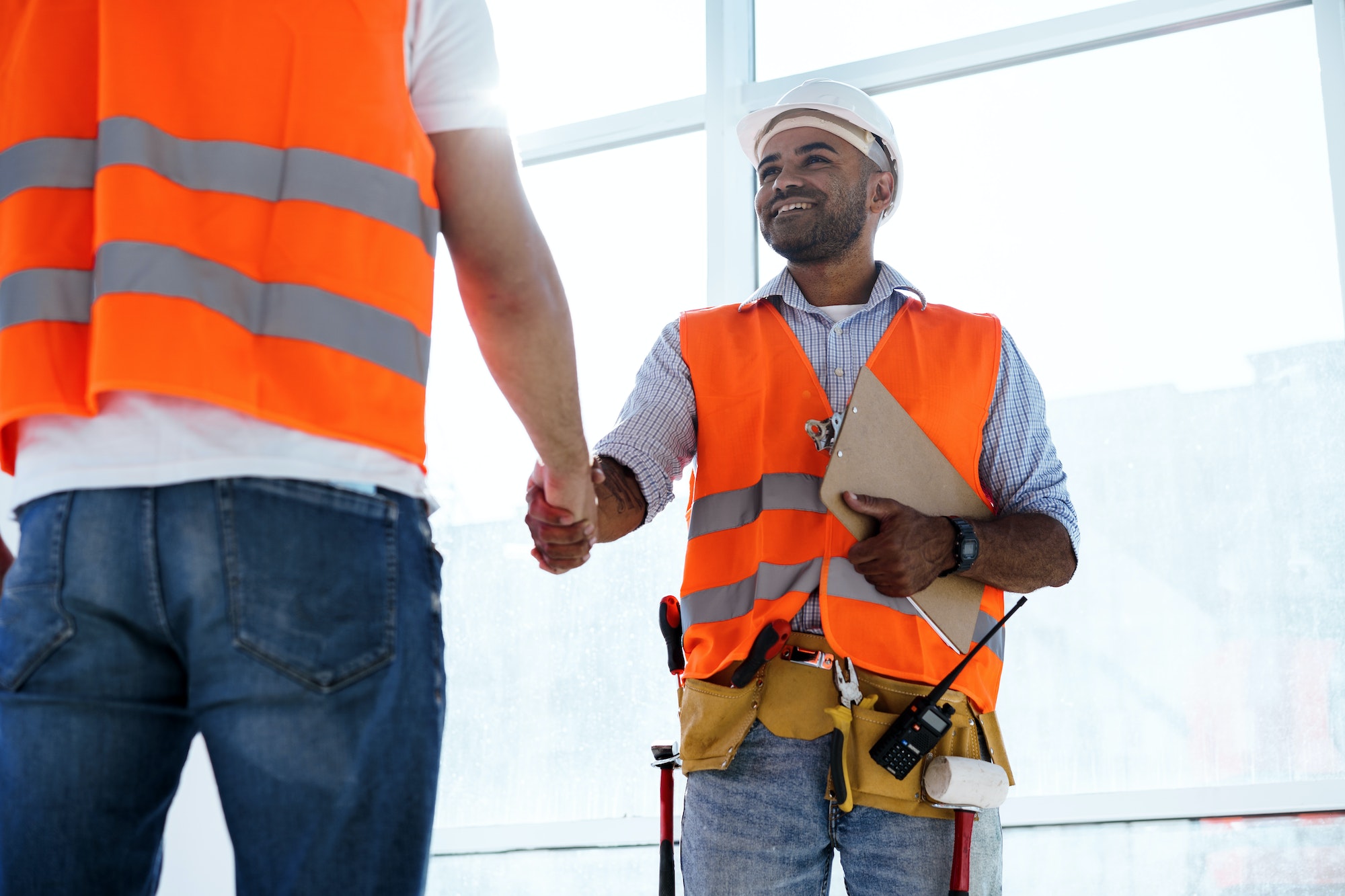 Two men engineers in workwear shaking hands against construction site
